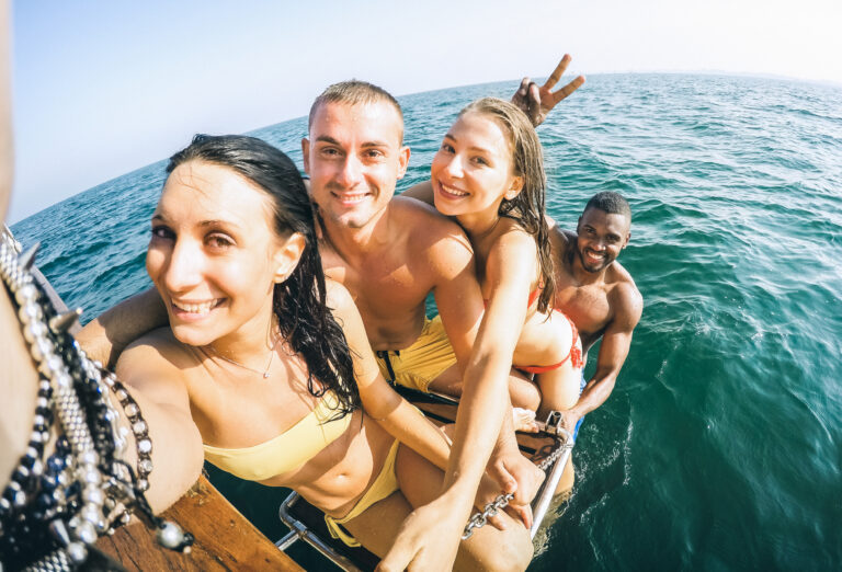 Young multiethnic friends taking selfie after swimming on sailing boat sea trip - Rich happy guys and girls having fun in summer party day - Exclusive vacation concept - Bright warm  vintage filter